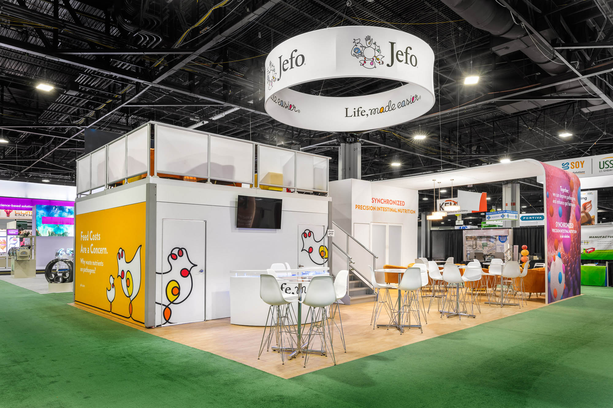 Large custom trade show exhibit featuring a double-deck booth design and branded overhead hanging sign